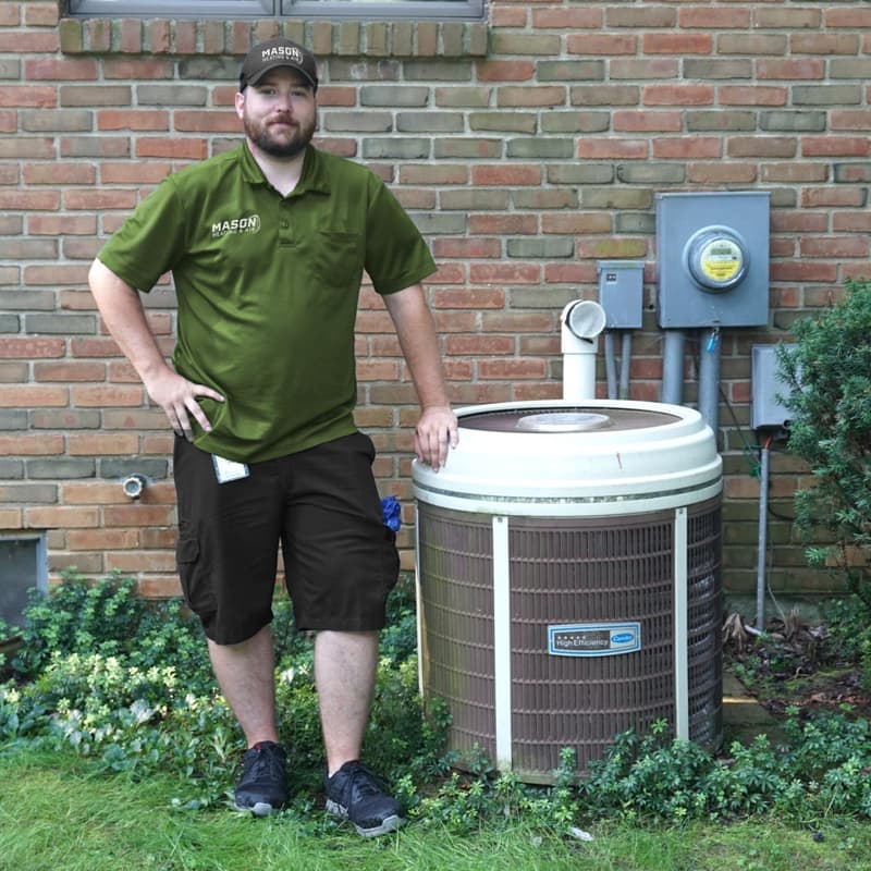 Technician standing beside outdoor condenser at brick house